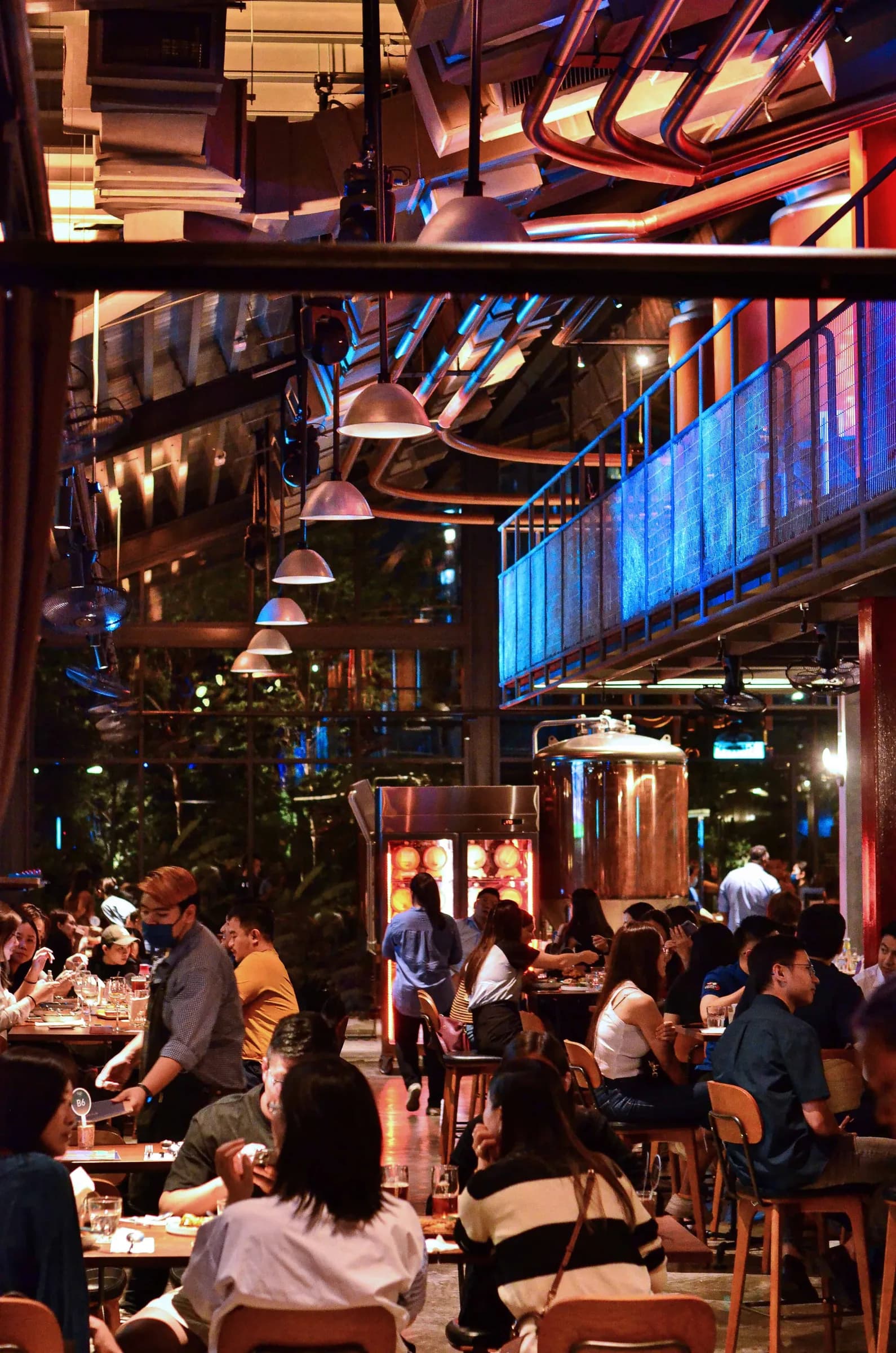 A bustling restaurant scene in a modern setting, featuring warm lighting, diners enjoying meals, and a bar area with brewing equipment in the background.
