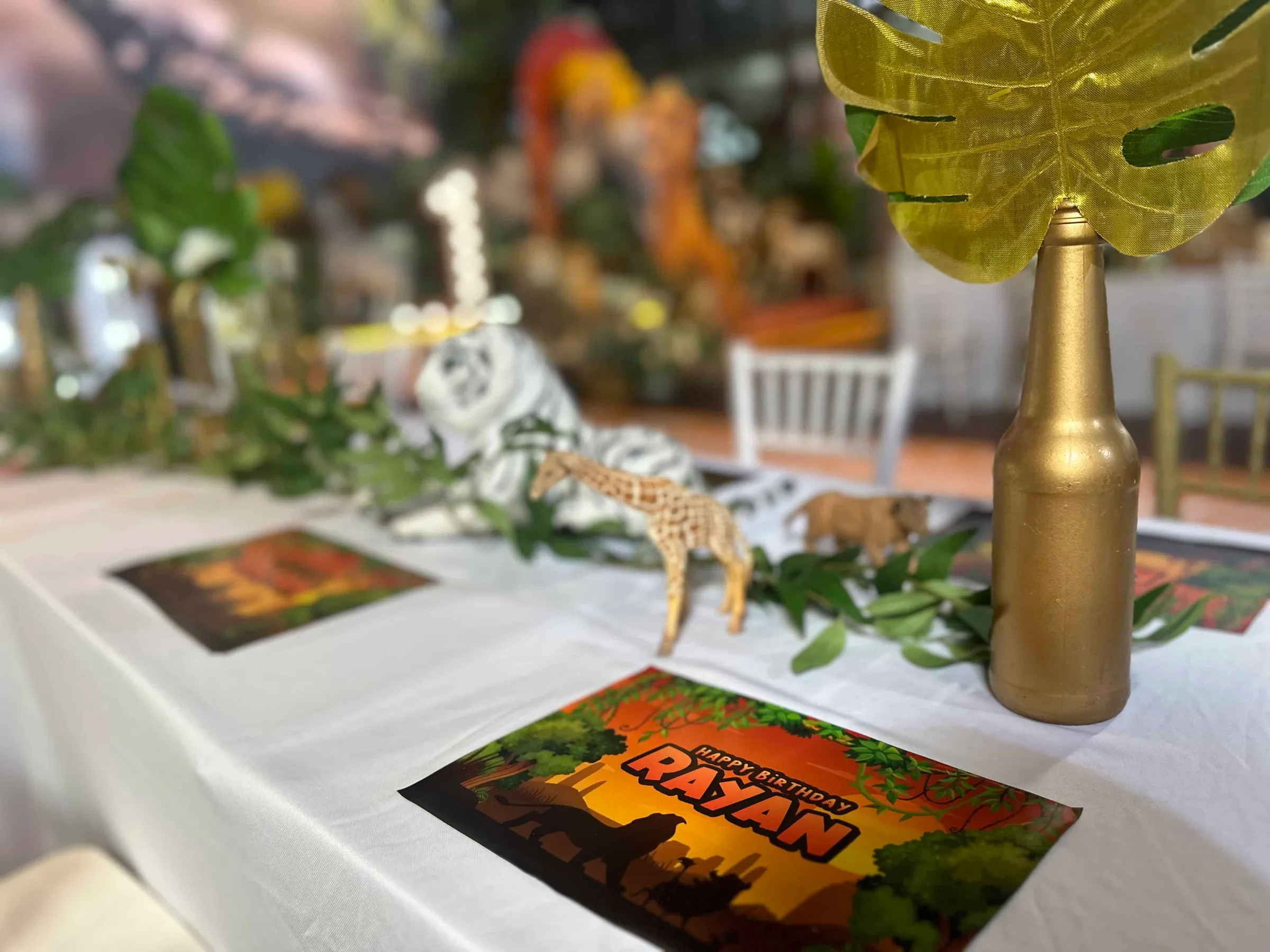 A decorated table set for a birthday party, featuring themed placemats, greenery, and decorative animal figurines.