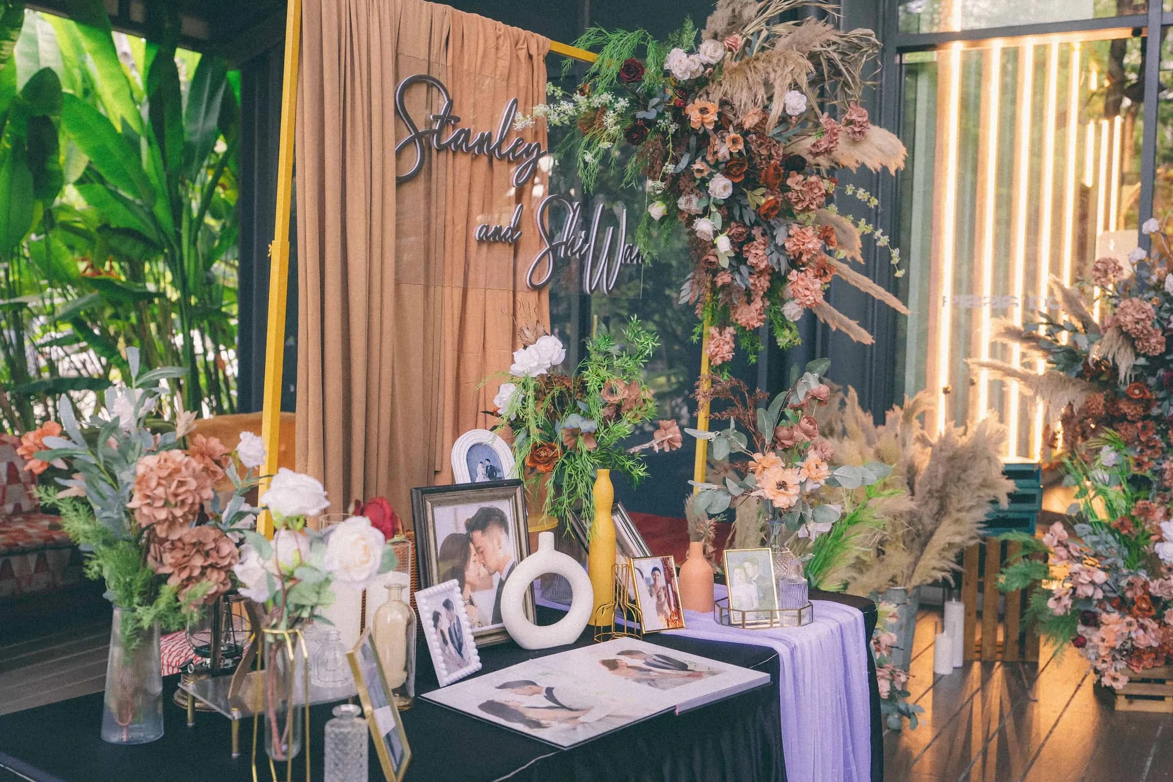 Wedding reception photo display table with floral arrangements and elegant fabric backdrop